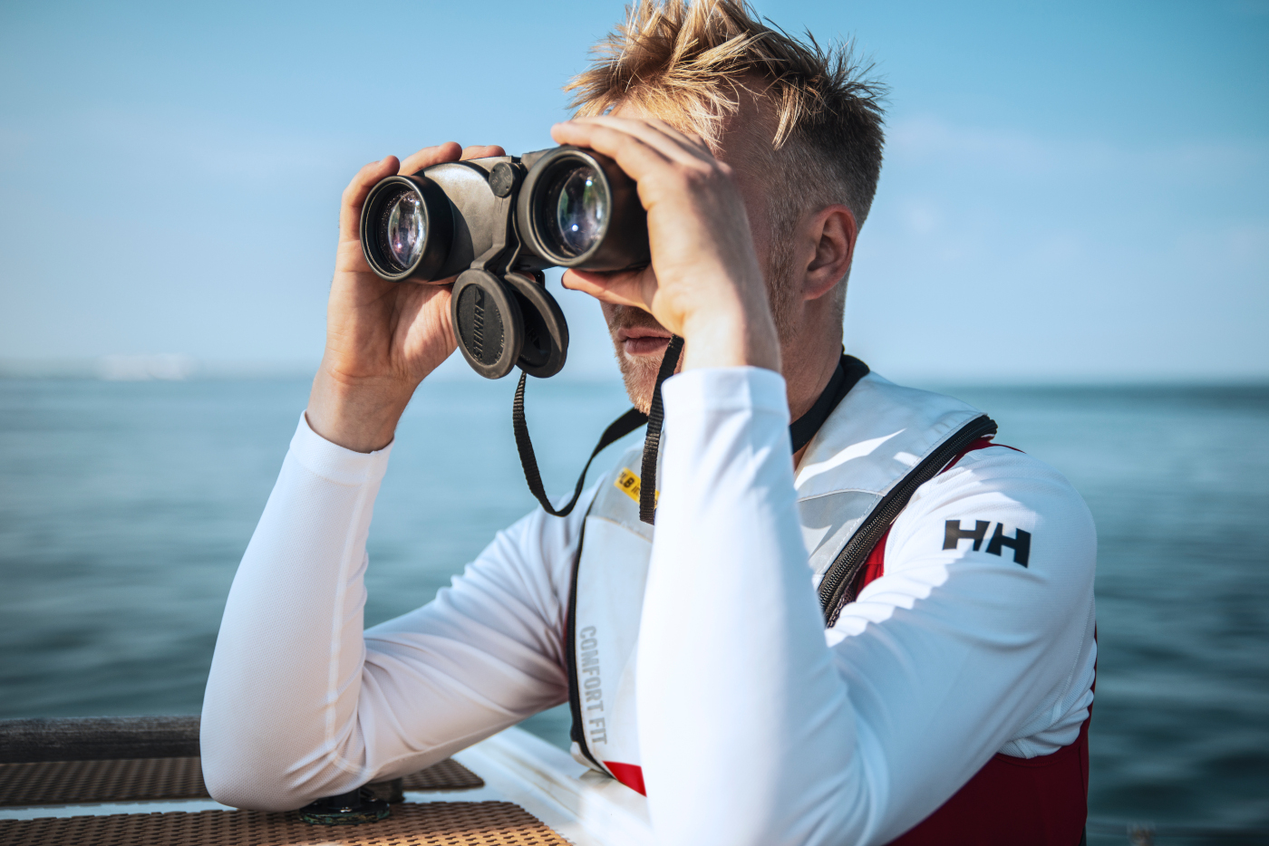 A Sea Ranger posing with binoculars, looking out to sea. In the background you can see the blue ocean and blue sky.