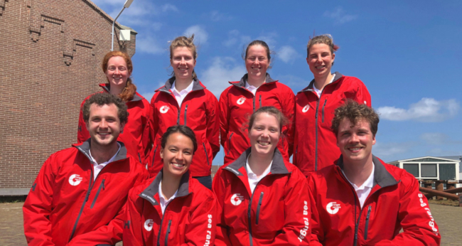 A team of eight Sea Rangers in red Sea Ranger uniforms posed in two rows of four. There are four female Sea Rangers standing up in the back row, and two male and two female Sea Rangers kneeling down in the front row. All are smiling and look happy.