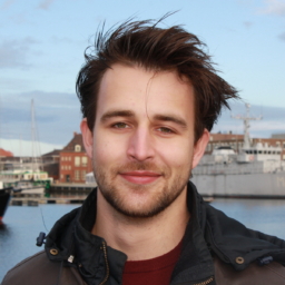 A headshot of Thierry van Veggel. Thierry is smiling at the camera. The sky behind him is blue.