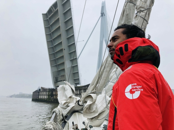 A Sea Ranger in red uniform is looking out to sea from a sailing boat.
