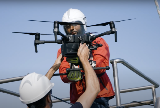 Two Sea Rangers on a boat, out at sea, setting up a drone to carry out ocean conservation work.