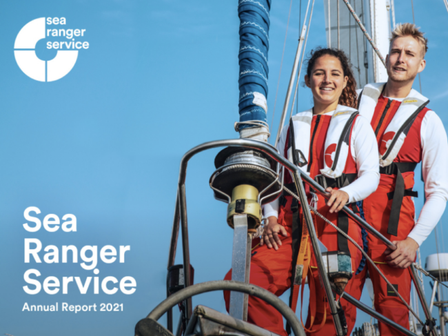 Front cover image of the Sea Ranger Service annual report 2021. Image is of two Sea Rangers posing at the front of a sailing ship.